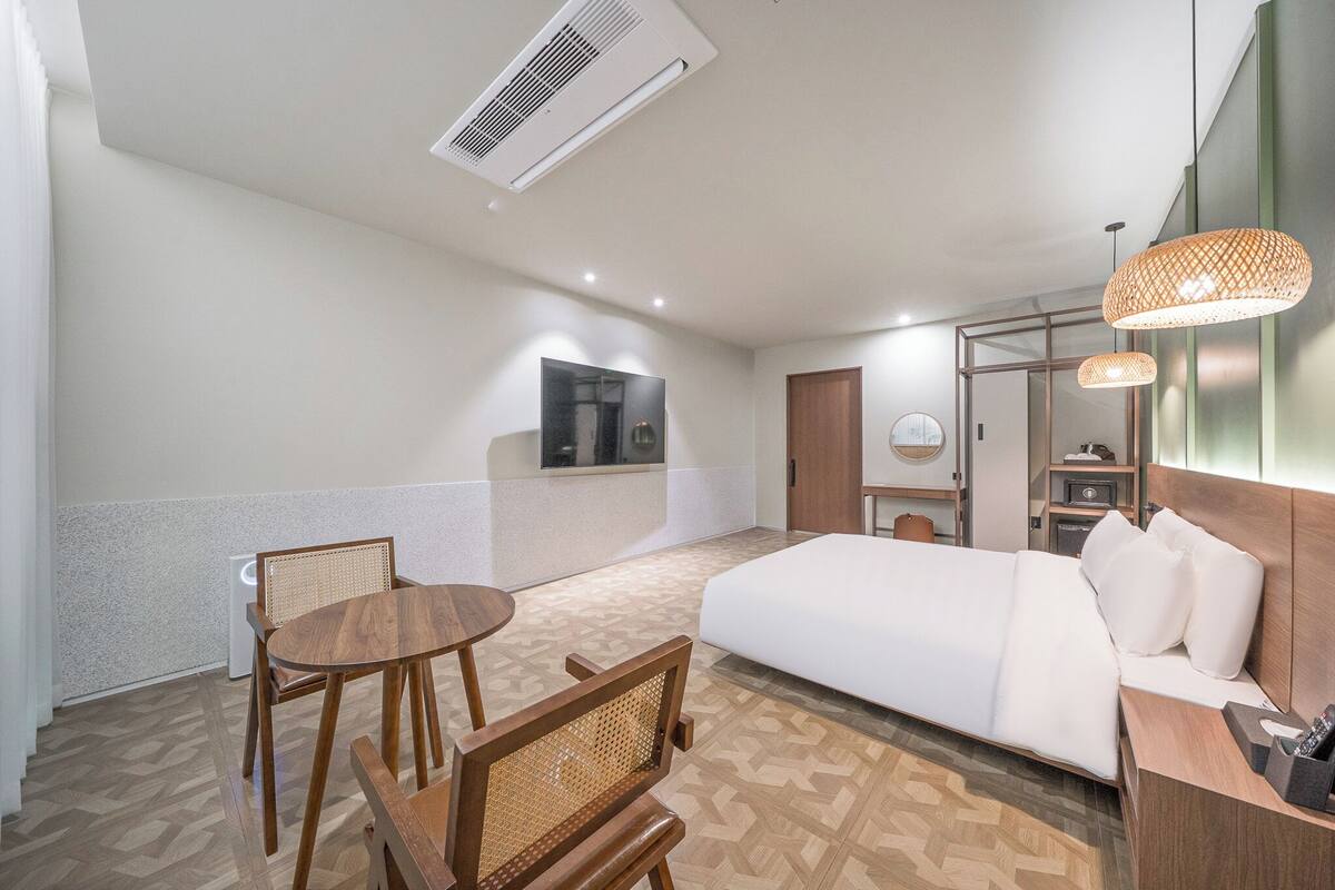 A hotel room with a bed, a desk, a chair, a table, and a mirror.