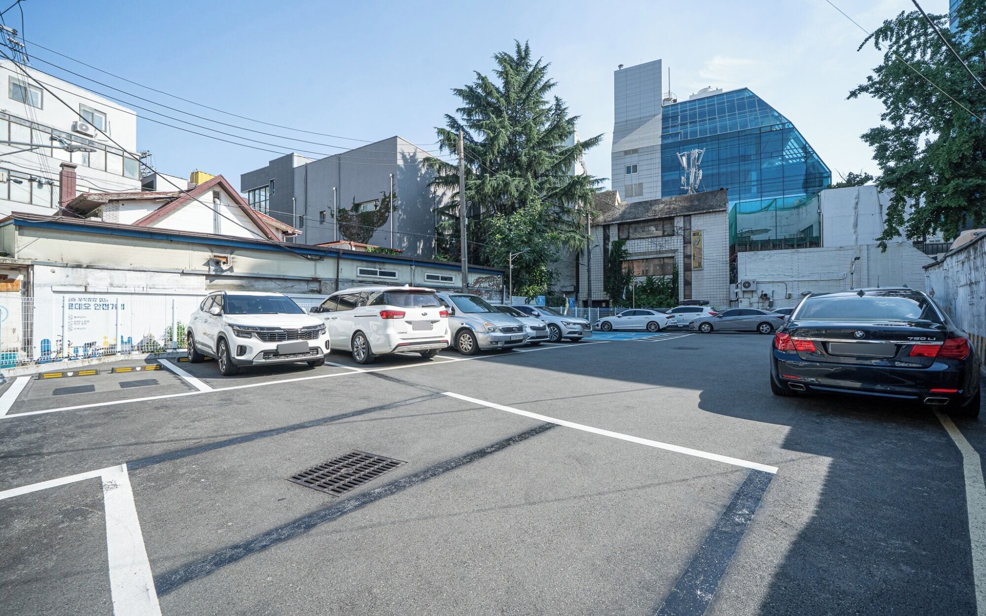 Un parcheggio con diverse automobili, un edificio con facciata in vetro moderno e un edificio tradizionale con tetto in tegole.