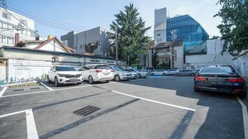 Un parcheggio con diverse automobili, un edificio con facciata in vetro moderno e un edificio tradizionale con tetto in tegole.