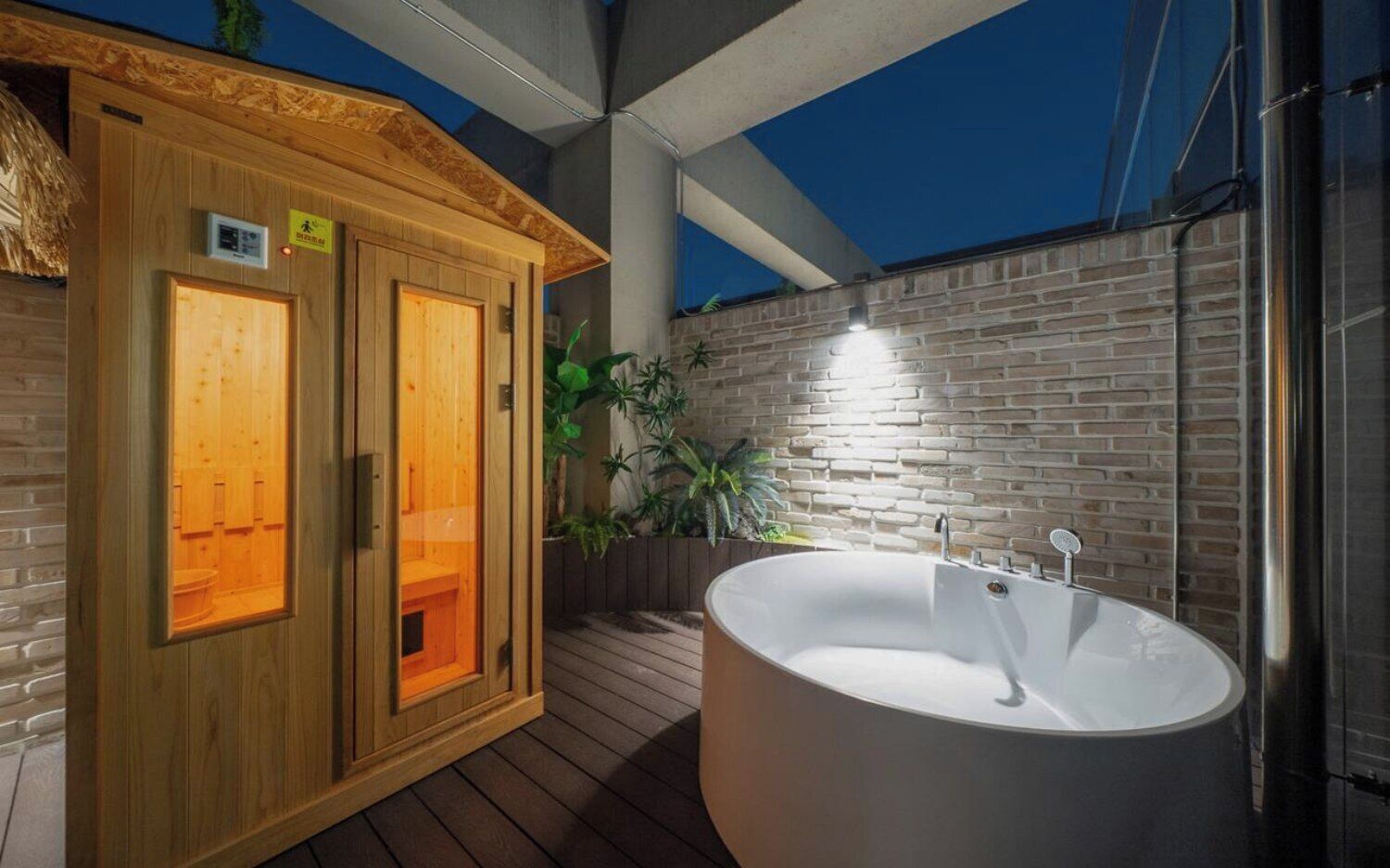 Una sauna de madera con puertas de vidrio, una bañera independiente grande y una pared de ladrillo.