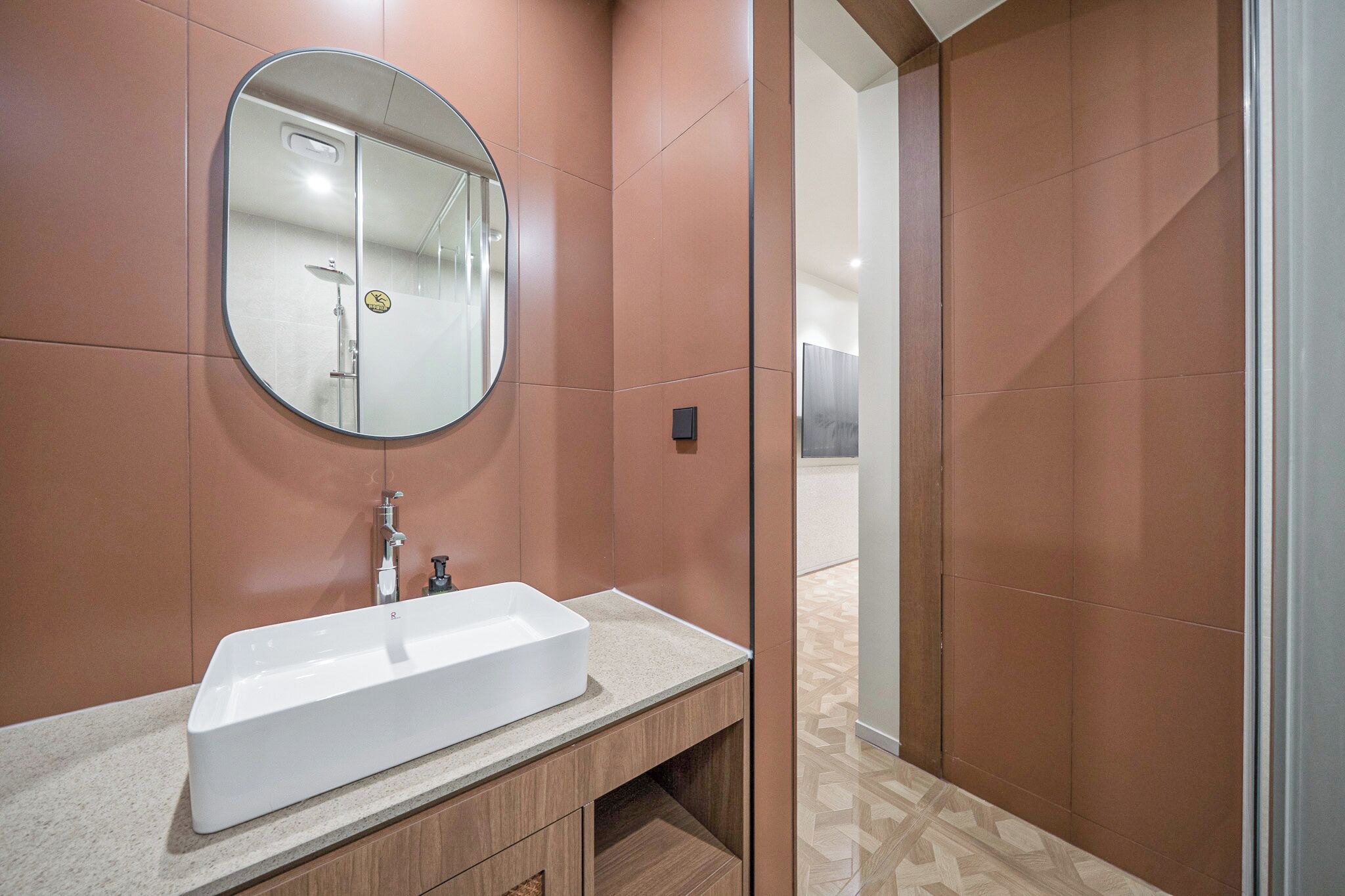 A modern bathroom with a rectangular sink, a round mirror, and a shower area.