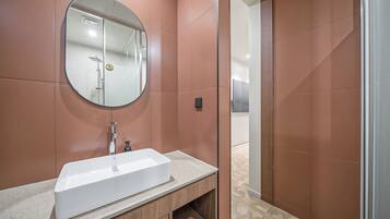 A modern bathroom with a rectangular sink, a round mirror, and a shower area.