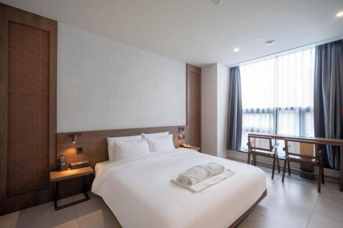 Ein Hotelzimmer mit einem großen Bett, Nachttischen, einem Schreibtisch und einem Fenster mit Vorhängen.