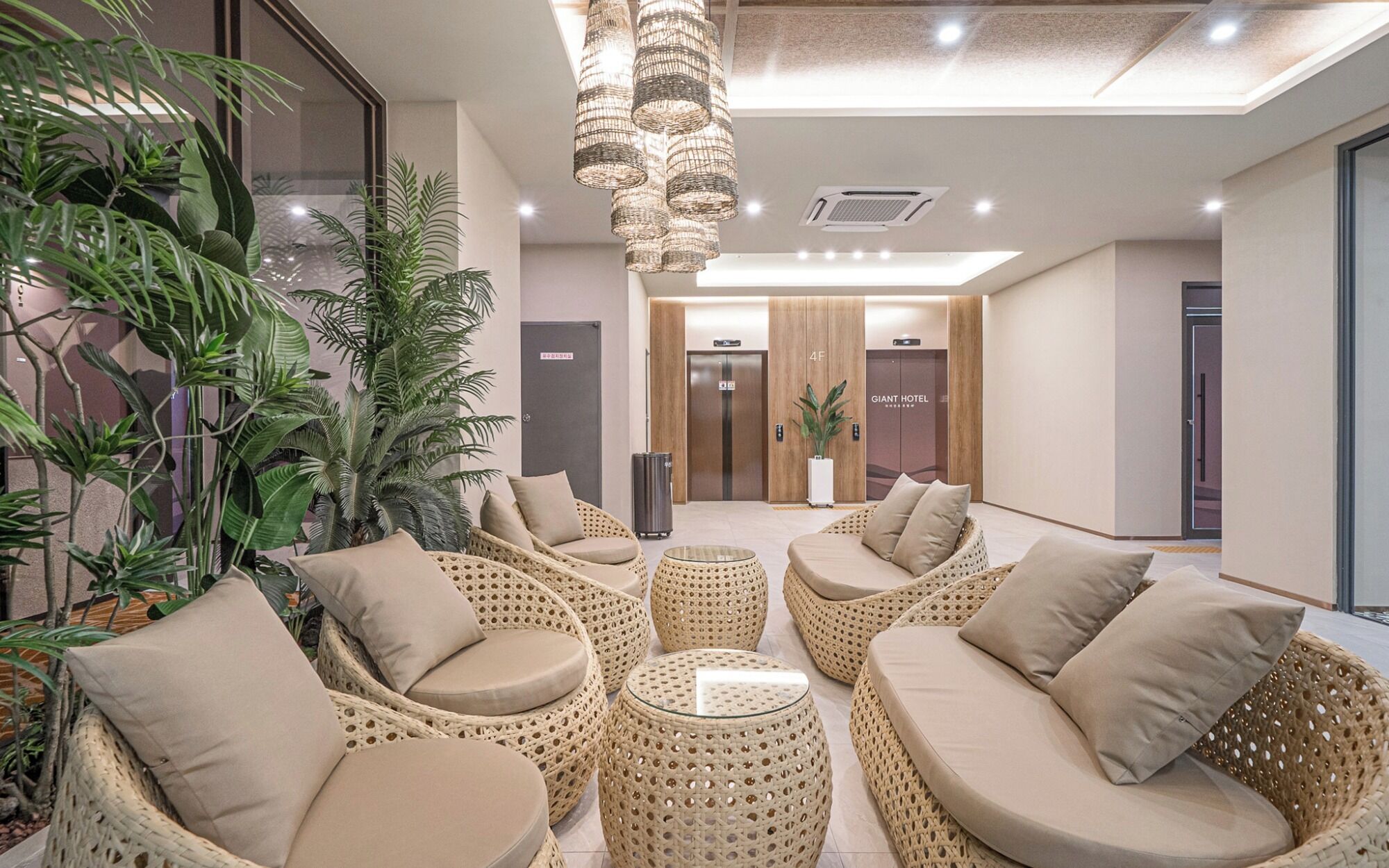 Un hall de hotel con mobiliario de mimbre, una mesa de centro de vidrio y una zona de recepción con una planta.