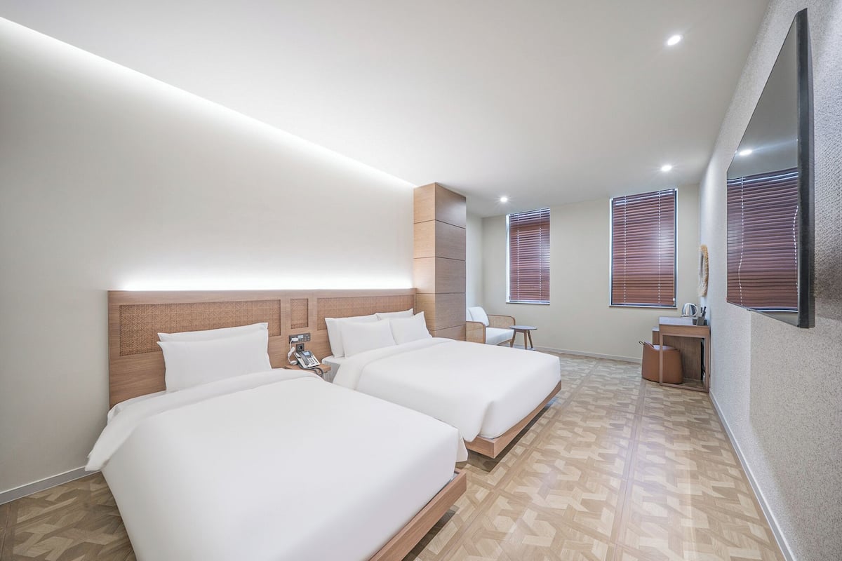 A modern hotel room with two beds, a desk, and a seating area.