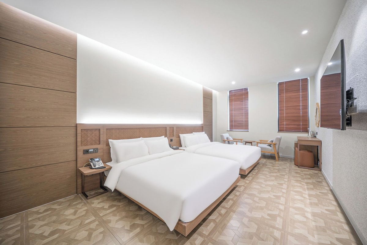 A modern hotel room with two beds, a desk, and a chair.