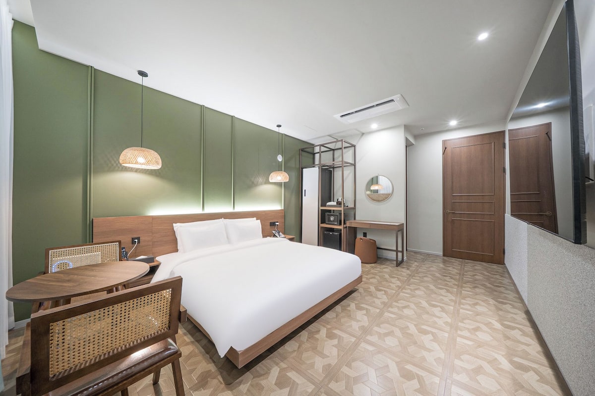A hotel room with a bed, a desk, a chair, a wardrobe, and a television.