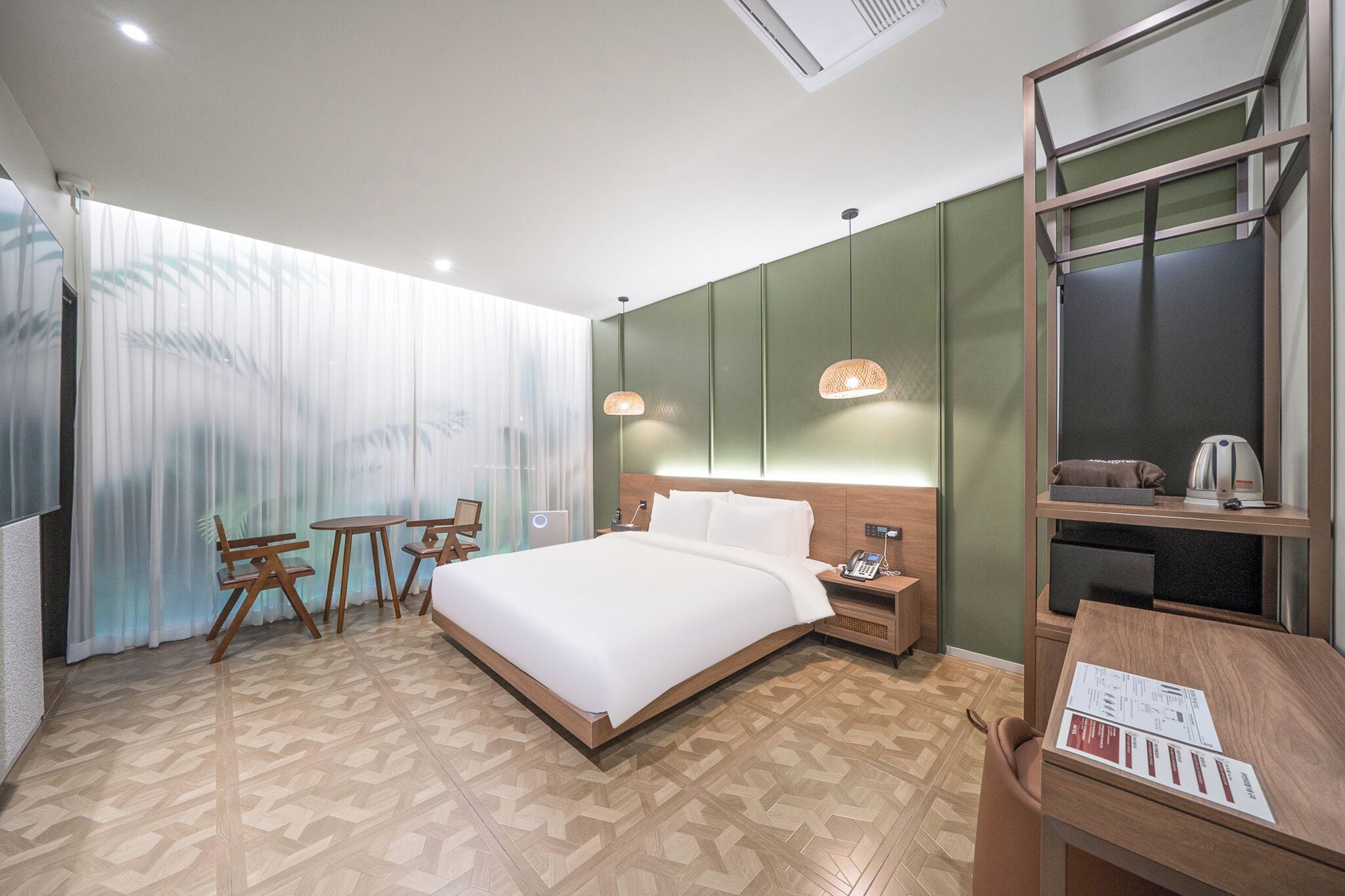 A hotel room with a large bed, a desk, a chair, a small table, and a nightstand.