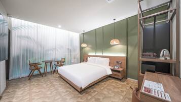 A hotel room with a large bed, a desk, a chair, a small table, and a nightstand.