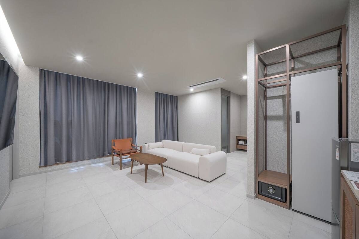 A modern living room with a white sofa, a wooden coffee table, and a small orange chair. There is a built-in cabinet with a lock on the right side.