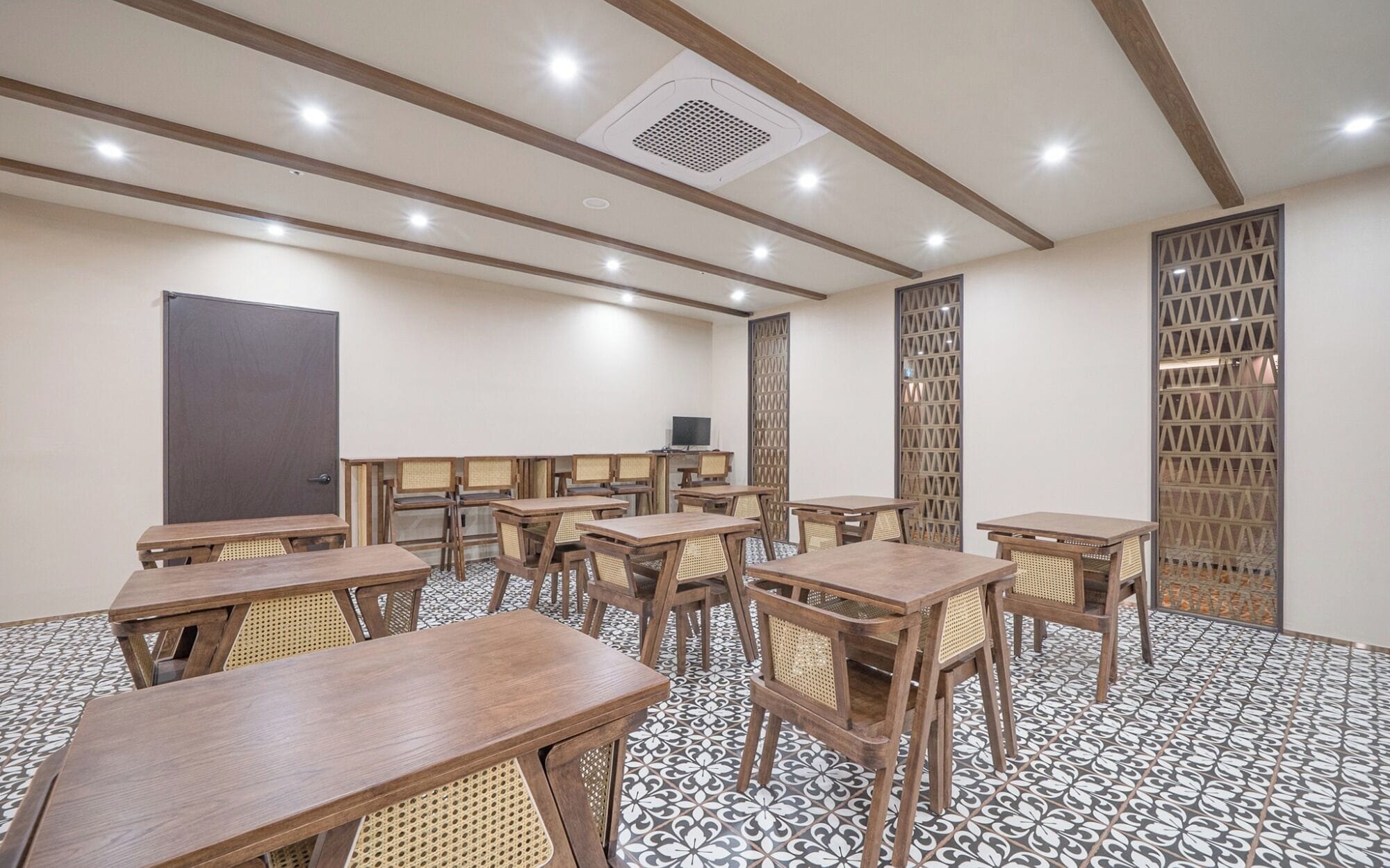 Un salón de conferencias con varias mesas y sillas, una pantalla de proyector y un suelo con diseño.