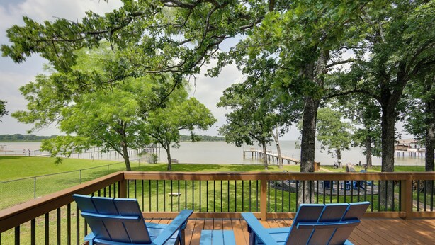 Een terras met blauwe stoelen en een tafel, met uitzicht op een meer met bomen en een steiger.