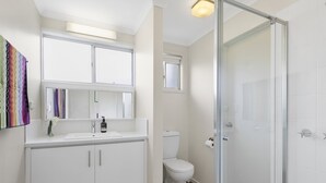 A modern bathroom with a white sink, mirror, and toilet. There is a shower area with a glass door.