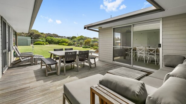 A modern patio with a wooden deck, outdoor furniture, and a view of a lush garden and hills in the background.