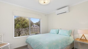A bedroom with a bed, a chair, a bedside table, a lamp, and a window with a view of a fence and trees.
