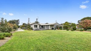 A single-story house with a covered porch, a lawn, and surrounding vegetation.