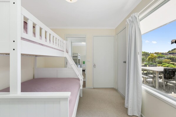 Ein Zimmer mit Etagenbetten, einer Tür und Blick auf einen Außenbereich mit Tischen und Stühlen.