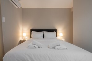 Ein ordentlich bezogenes Bett mit weißen Leinentüchern und zwei gefalteten Handtüchern am Fußende. Auf jeder Seite des Bettes stehen je eine Nachttischlampe.
