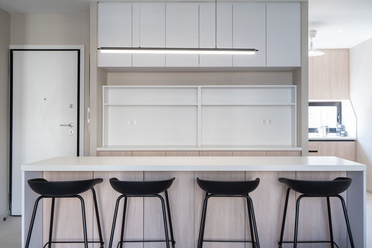 A modern kitchen with white cabinetry, a white countertop, and three black bar stools.