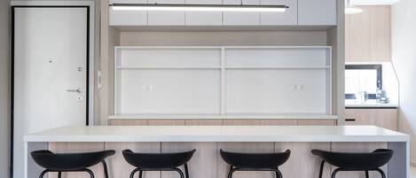 A modern kitchen with white cabinetry, a white countertop, and three black bar stools.