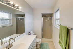 Ein Badezimmer mit weißem Waschbecken, Spiegel und Toilette, einer Dusche mit Glastür und einem grünen Handtuch an der Wand.