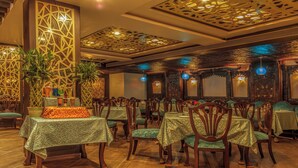 Un restaurante con varias mesas y sillas, paneles decorativos en la pared y lámparas colgantes.