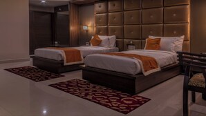 Habitación de hotel con dos camas, un cabecero grande y acolchado, un espejo y una silla de madera.