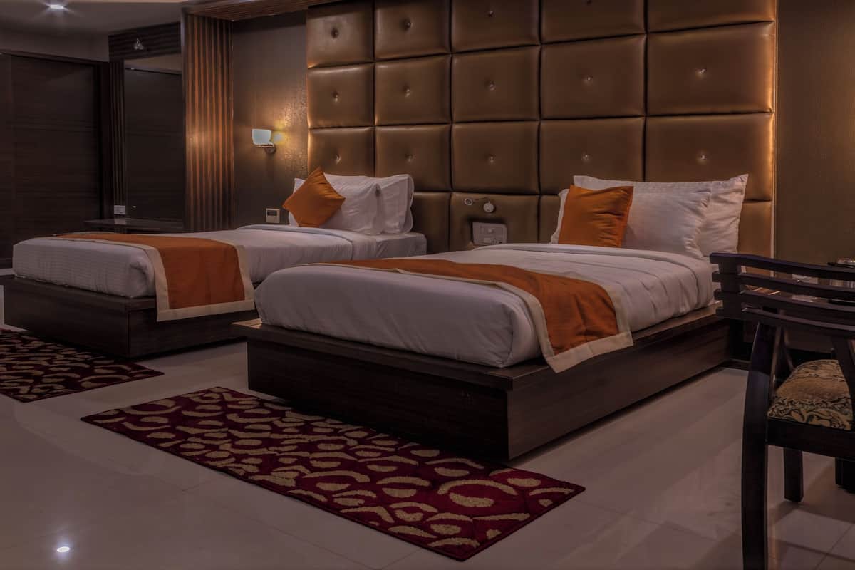 Habitación de hotel con dos camas, un cabecero grande y acolchado, un espejo y una silla de madera.