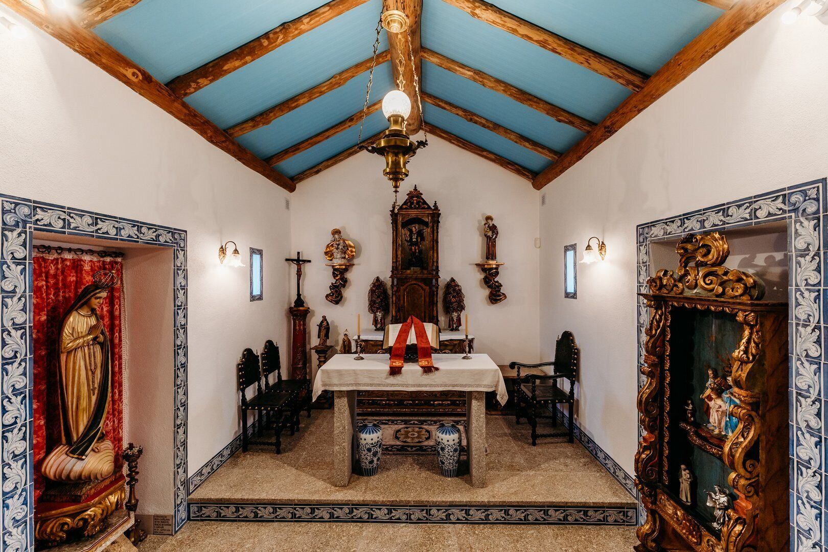 Una habitación con techo de madera, una mesa central con mantel blanco y una estatua de un personaje religioso a la izquierda.