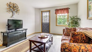 A living room with a TV, dark wooden entertainment unit, patterned sofa, and a door with a window.