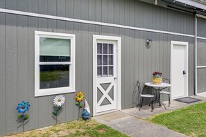 Un bâtiment gris avec une porte blanche, une fenêtre avec des stores et un petit jardin agrémenté d’une table et de chaises.