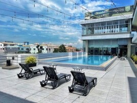Un área de piscina en la azotea con sillones de descanso y un edificio moderno al fondo.