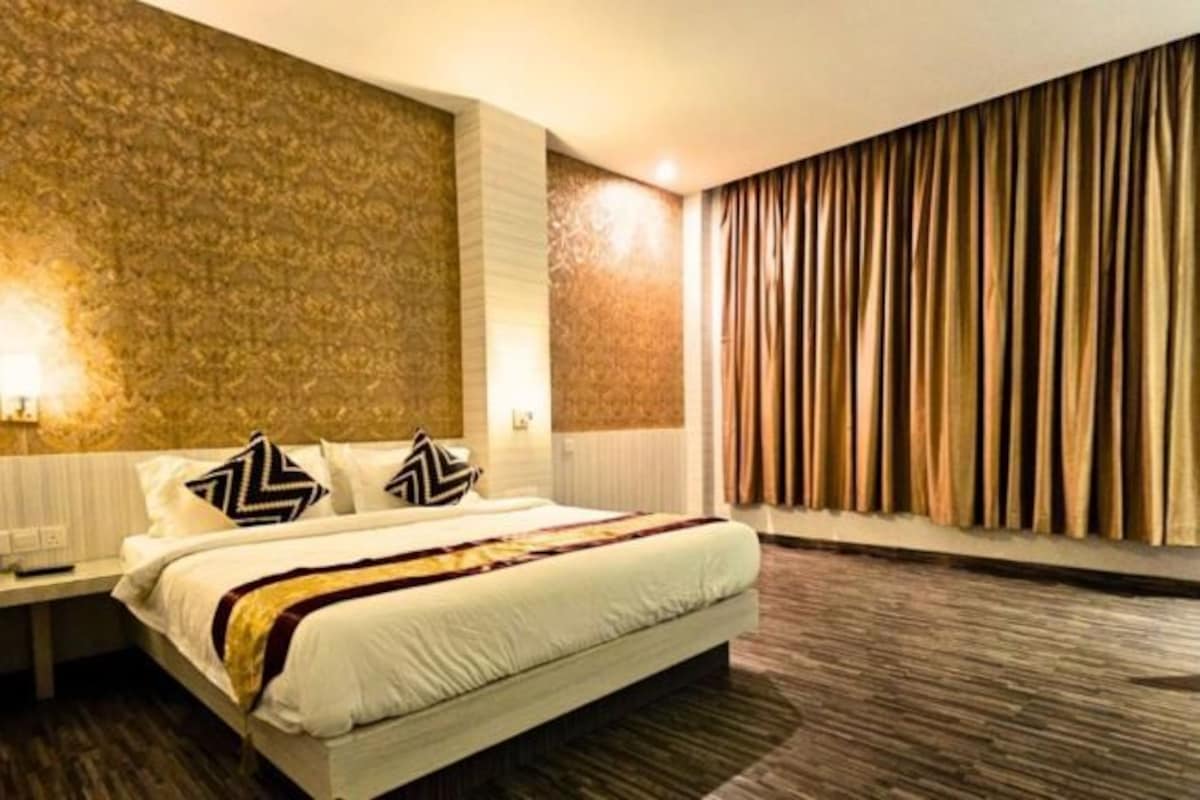 A hotel room with a large bed, a nightstand, a wall with a patterned design, and a curtain on the window.