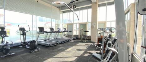 A gym with treadmills, weight machines, and a large window providing a view of the outside.