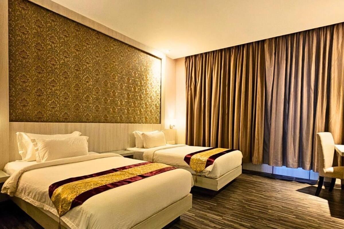 A hotel room with two beds, a patterned wall, and a large window with curtains.