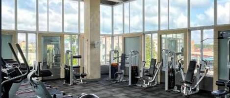 Un gimnasio con equipamiento de ejercicio, ventanas amplias y vistas a la ciudad.