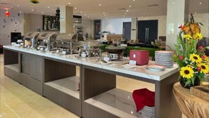 Een moderne buffetopstelling met meerdere thematafels, een centraal bedieningspunt en decoratieve details zoals lantaarns in de vorm van ananas en een bloemstuk.