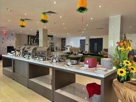 Una moderna disposición de bufé con múltiples estaciones de comida, un área central de servicio y elementos decorativos como luces con forma de piña colgantes y un arreglo floral.