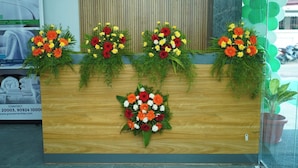 A reception desk with four flower arrangements, a contact number, and a website address. - Grace Vista (Thanjavur)