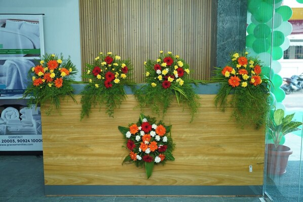 A reception desk with four flower arrangements, a contact number, and a website address. - Grace Vista (Thanjavur)
