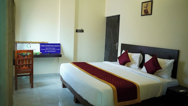 A hotel room with a bed, a desk, and a chair. There is a sign on the desk with the hotel's name and contact information. - Grace Vista (Thanjavur)