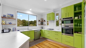 A modern kitchen with green cabinets, a white countertop, and a large window offering a view of trees. - Quiet Ninderry Cottage with Peaceful Rural Outlook (Ninderry)