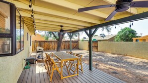 Una veranda coperta con tavolo e sedie in legno, una ventola a soffitto e vista sul giardino.