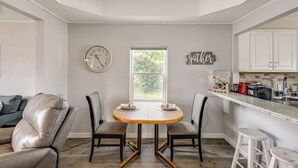 A modern kitchen with a dining table, two chairs, a clock, and a window with a view of greenery. - Quaint Home 16 Mi to Bear Lake: Fish, Hike & Bike! (Montpelier)