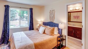Une chambre à coucher avec un lit, une table de chevet, une commode et une fenêtre avec des rideaux.