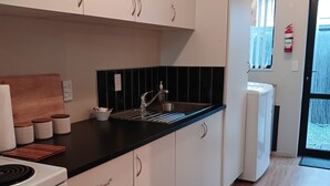 A modern kitchen with white cabinets, a black countertop, and a stainless steel sink. There is a stove, a microwave, and a small refrigerator. A checkered towel hangs on the oven handle. - Simple and Sweet in Queenstown (Lake Hayes Estate)