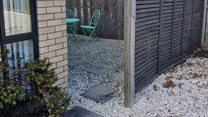 A patio area with a brick wall, a metal frog decoration, a green metal chair, and a wooden fence. - Simple and Sweet in Queenstown (Lake Hayes Estate)