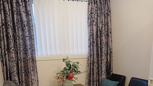A dining area with a wooden table, four chairs, a vase with a plant, and a window with curtains. - Simple and Sweet in Queenstown (Lake Hayes Estate)