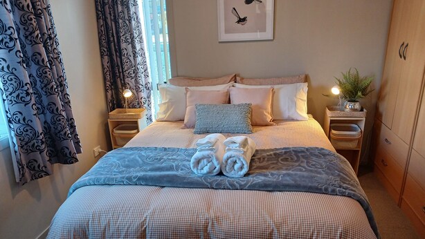 A neatly made bed with checkered bedding, two rolled towels, and a decorative pillow. - Simple and Sweet in Queenstown (Lake Hayes Estate)