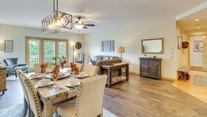 A spacious living room with a wooden dining table, comfortable seating, a ceiling fan, and a large window offering a view of the outdoors. - 2 Mi to Angel Fire Resort: Luxury Condo w/ Balcony (Angel Fire)